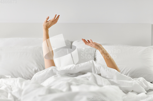 Image of hands of woman lying in bed and stretching