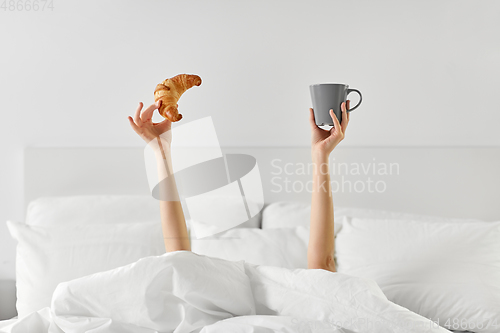 Image of woman with coffee and croissant lying in bed