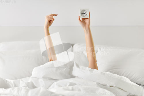 Image of hands of woman lying in bed with alarm clock