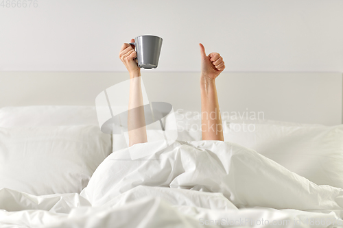 Image of woman with coffee lying in bed showing thumbs up