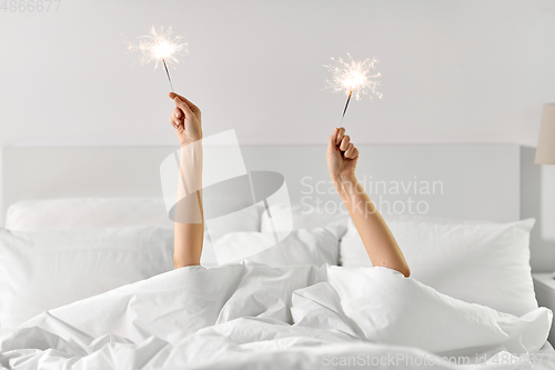 Image of hands of woman lying in bed with sparklers