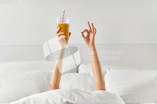 Image of hands of woman lying in bed with cup of juice