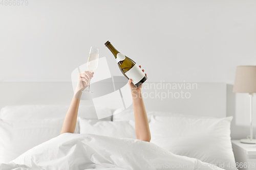 Image of hands of woman lying in bed with champagne