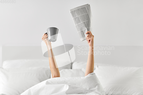 Image of woman with coffee and newspaper lying in bed