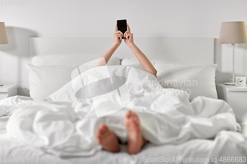 Image of hands of woman lying in bed with smartphone