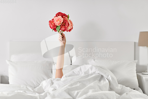 Image of hand of woman lying in bed with bunch of flowers