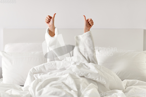 Image of hands of woman lying in bed and showing thumbs up