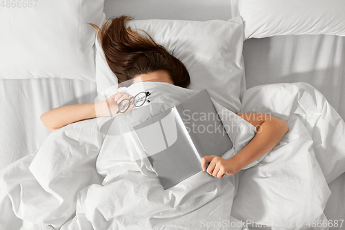 Image of woman lying in bed with book and glasses