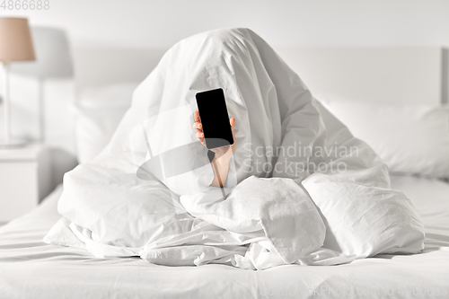 Image of woman with phone sitting under blanket in bed