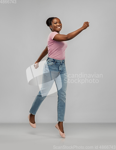 Image of happy african american woman jumping over grey