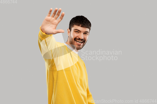 Image of smiling young man in yellow sweatshirt waving hand