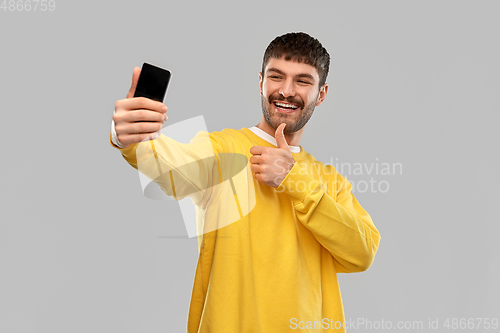 Image of man takes selfie with phone and shows thumbs up