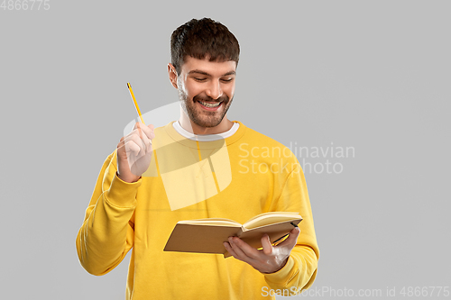 Image of happy man in yellow sweater with diary and pencil