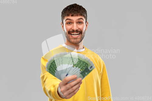 Image of smiling young man in yellow sweatshirt with money