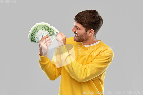 Image of smiling young man in yellow sweatshirt with money