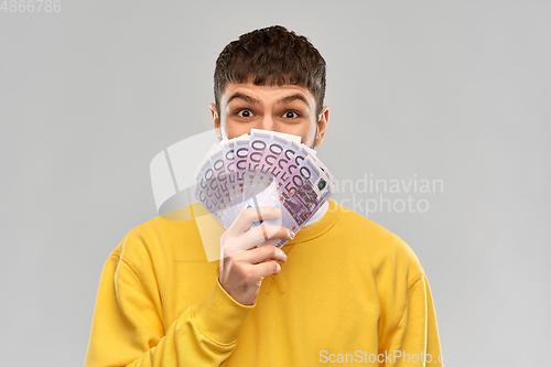 Image of happy young man in yellow sweatshirt with money