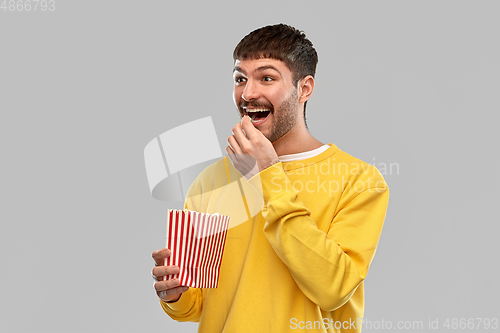 Image of smiling man in yellow sweatshirt eating popcorn