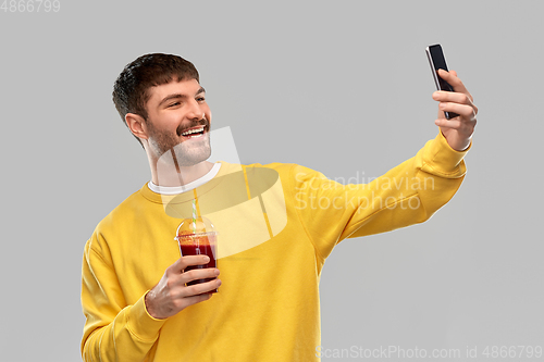 Image of happy man with smartphone and juice taking selfie