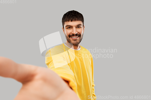 Image of happy young man in yellow sweatshirt making selfie