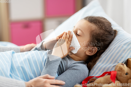 Image of mother and ill little daughter blowing nose in bed