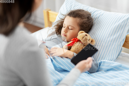 Image of sleeping daughter and mother with phone at home