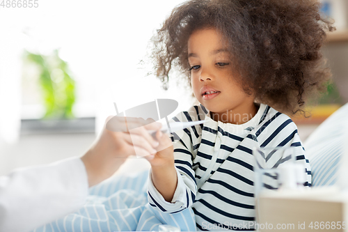 Image of doctor showing thermometer to smiling sick girl