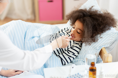 Image of doctor giving medicine to sick girl in bed at home