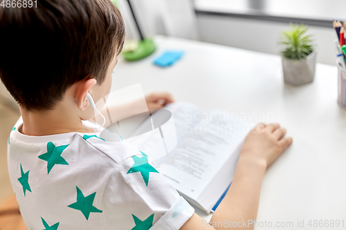 Image of boy with earphones and textbook learning at home