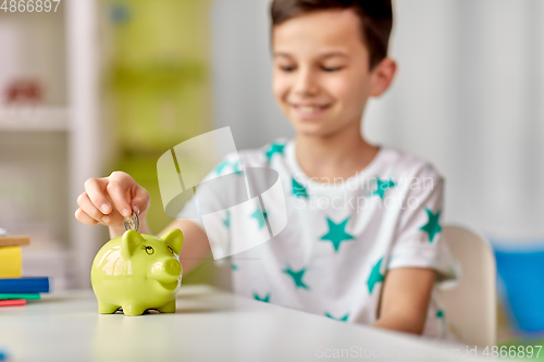 Image of little boy putting coin into piggy bank at home