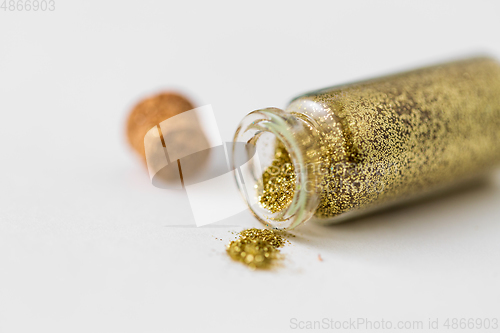 Image of golden glitters poured from small glass bottle