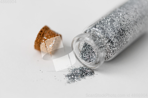 Image of silver glitters poured from small glass bottle
