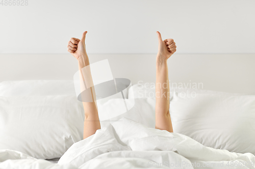 Image of hands of woman lying in bed and showing thumbs up