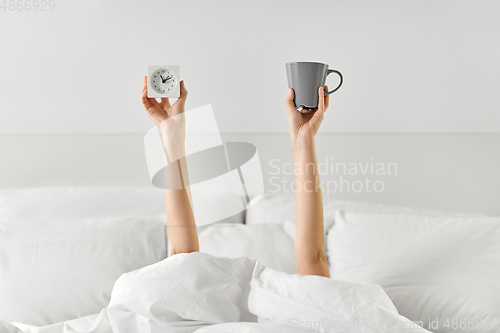 Image of woman with coffee and alarm clock lying in bed