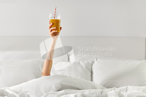 Image of hand of woman lying in bed with cup of juice