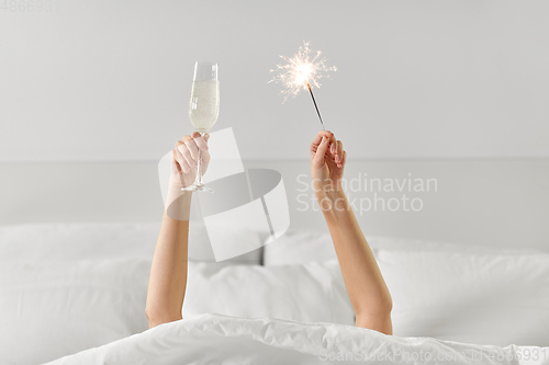 Image of hands of woman in bed with champagne and sparkler