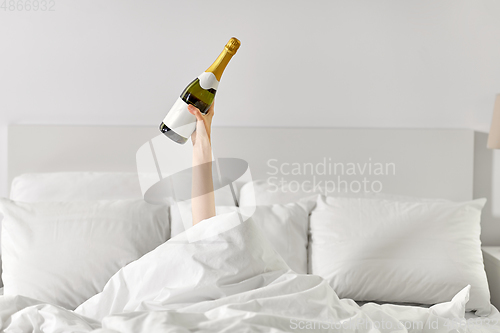 Image of hand of woman lying in bed with champagne