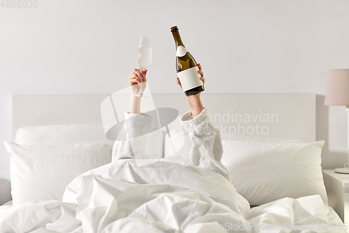 Image of hands of woman lying in bed with champagne