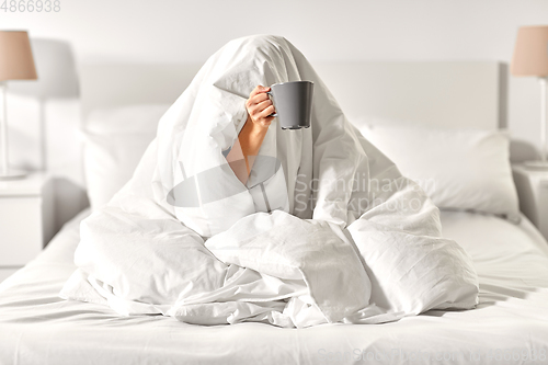 Image of woman with coffee sitting under blanket in bed