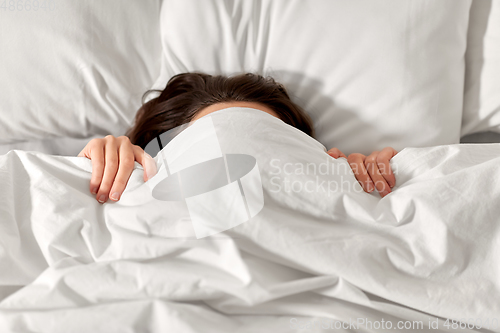 Image of woman lying in bed under white blanket or duvet