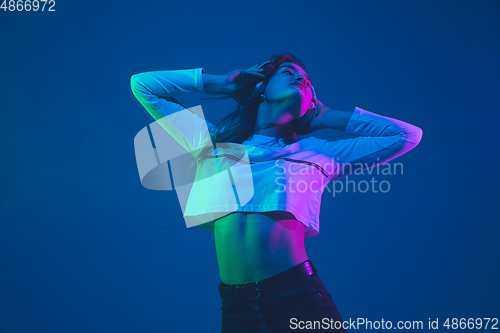 Image of Caucasian woman\'s portrait isolated on blue studio background in pink-green neon light, stylish and beautiful