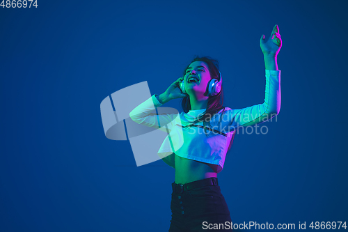 Image of Caucasian woman\'s portrait isolated on blue studio background in pink-green neon light, stylish and beautiful