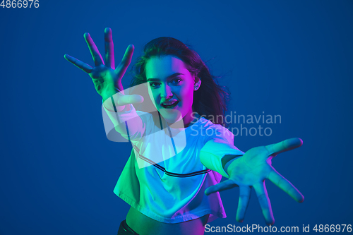 Image of Caucasian woman\'s portrait isolated on blue studio background in pink-green neon light, stylish and beautiful