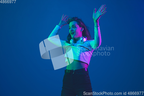 Image of Caucasian woman\'s portrait isolated on blue studio background in pink-green neon light, stylish and beautiful
