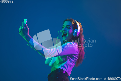 Image of Caucasian woman\'s portrait isolated on blue studio background in pink-green neon light, stylish and beautiful