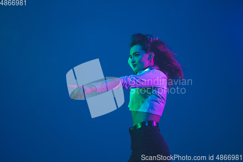 Image of Caucasian woman\'s portrait isolated on blue studio background in pink-green neon light, stylish and beautiful