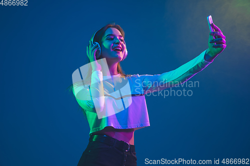 Image of Caucasian woman\'s portrait isolated on blue studio background in pink-green neon light, stylish and beautiful