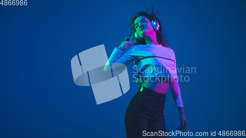 Image of Caucasian woman\'s portrait isolated on blue studio background in pink-green neon light, stylish and beautiful
