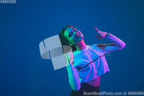 Image of Caucasian woman\'s portrait isolated on blue studio background in pink-green neon light, stylish and beautiful