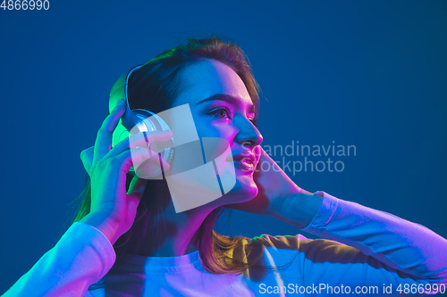 Image of Caucasian woman\'s portrait isolated on blue studio background in pink-green neon light, stylish and beautiful