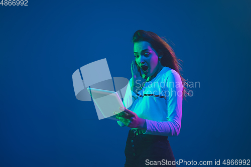 Image of Caucasian woman\'s portrait isolated on blue studio background in pink-green neon light, stylish and beautiful